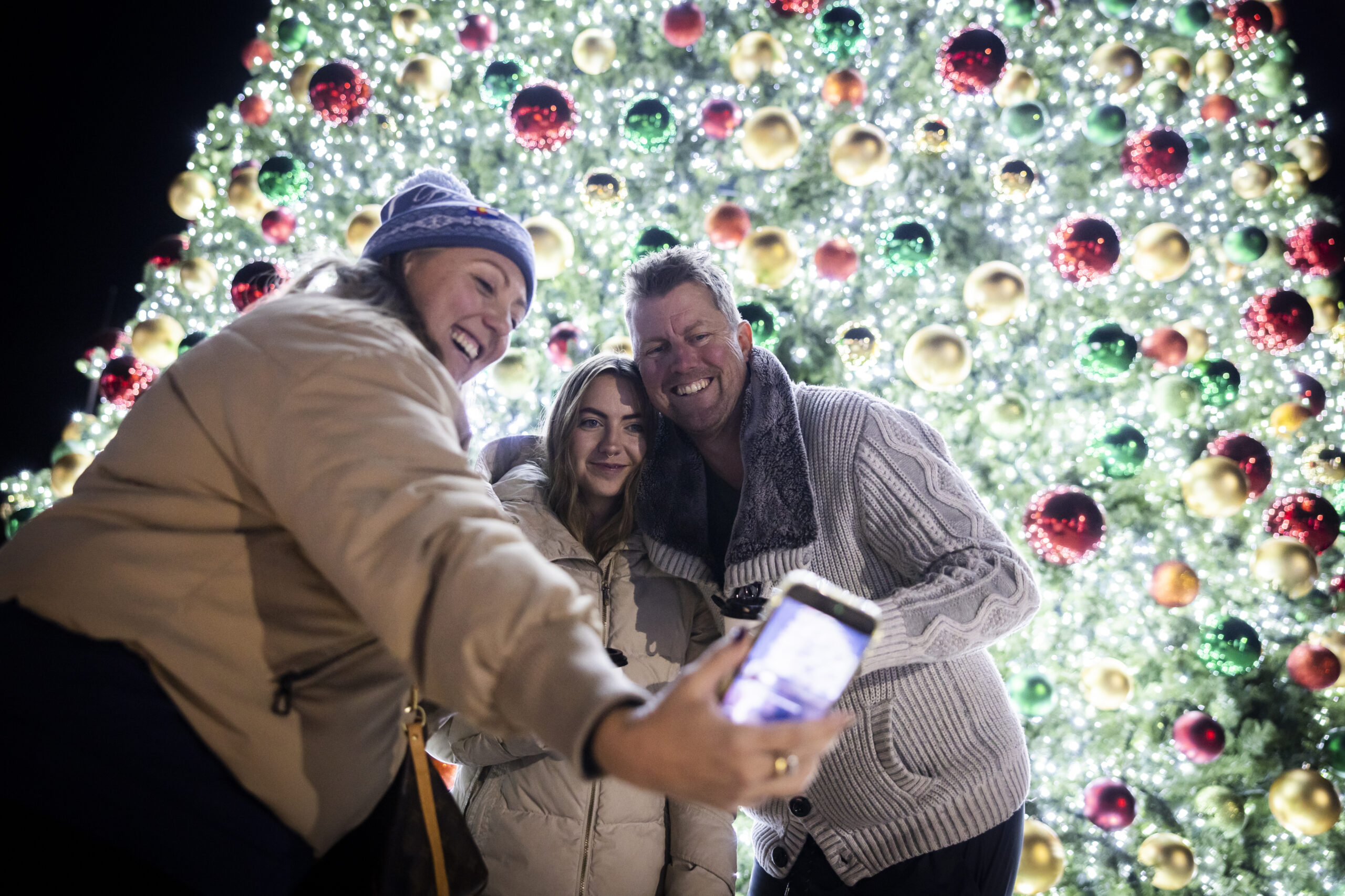 Three people take a holiday selfie in front of a decorated Christmas tree